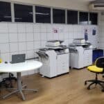 Fotografia da sala dos professores com mesas e máquinas de fotocópia